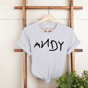 Może przedstawiać: Szary T-shirt z napisem "ANDY" napisanym czarnym markerem.