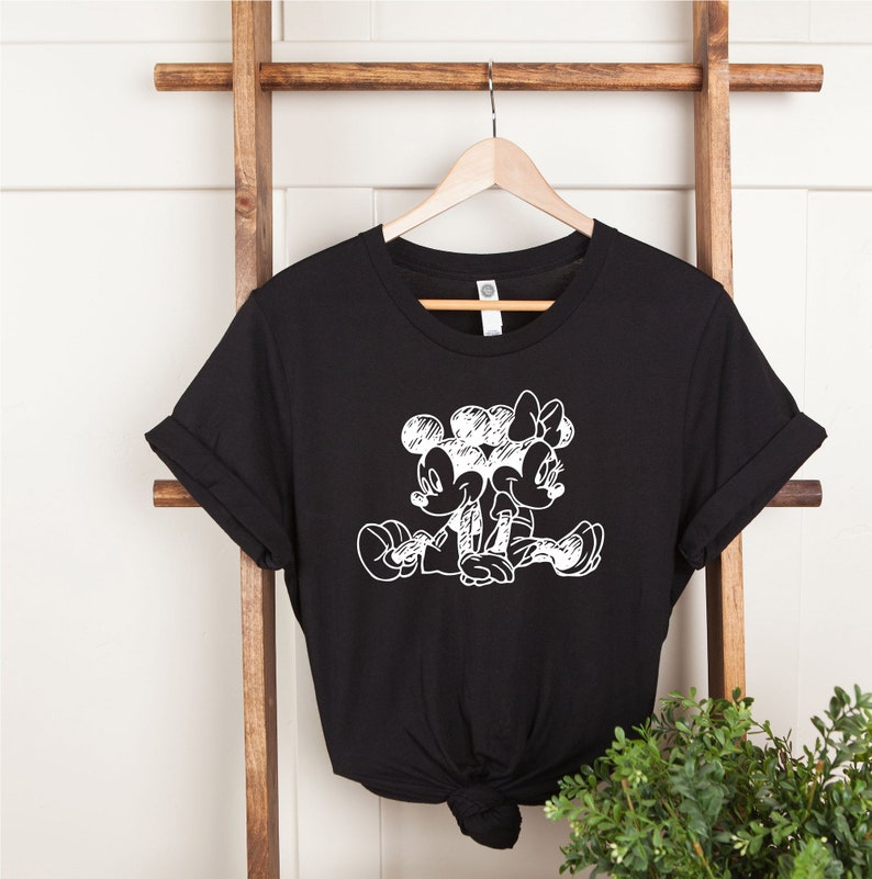 Puede incluir: Camiseta negra con un dibujo de contorno blanco de Mickey Mouse y Minnie Mouse tom&aacute;ndose de la mano.