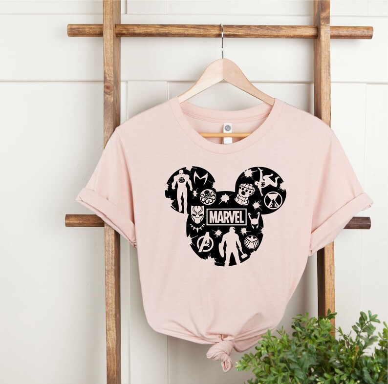 May include: A pink t-shirt with a black Mickey Mouse silhouette filled with Marvel characters and the word "MARVEL" in the center.