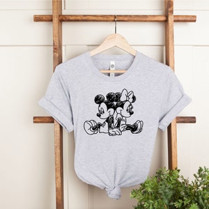 Puede incluir: Una camiseta gris con un boceto en blanco y negro de Mickey Mouse y Minnie Mouse sentados juntos.