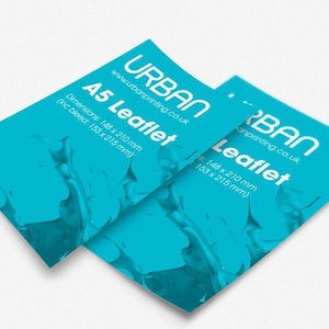 May include: Two A5 leaflets with a teal blue background and white text. The leaflets have the text "URBAN" and "Leaflet" printed on them, along with the website address and dimensions of 148 x 210 mm (5.8 x 8.3 inches).