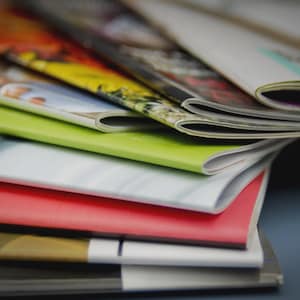 May include: A pile of magazines with vibrant covers. The covers showcase a range of colours, including red, green, yellow, and white. The magazines are stacked, with the pages slightly fanned out, creating a layered effect.