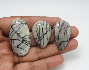 May include: Three polished gemstones in oval and teardrop shapes. The stones have a light gray base color with intricate black veining patterns. The gemstones are displayed against a neutral background.