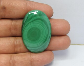 May include: Oval-shaped malachite gemstone with concentric green patterns. The polished stone displays varying shades of green, creating a swirling effect. The gemstone is smooth and reflects light, showcasing its natural beauty.