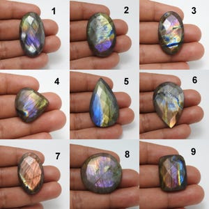 May include: Nine faceted labradorite gemstones in various shapes, including oval, teardrop, and square. The stones display iridescent flashes of blue, purple, and gold. Each stone is held in a hand, showcasing the natural beauty and unique patterns of the gemstones.