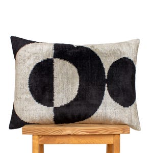 Könnte beinhalten: Ein rechteckiges Zierkissen mit einem geometrischen Design in Schwarz und Off-White. Das Kissen zeigt ein Muster aus sich überlappenden Kreisen, wobei eine Seite der Kreise schwarz und die andere off-white ist. Das Kissen liegt auf einem Holzschemel.