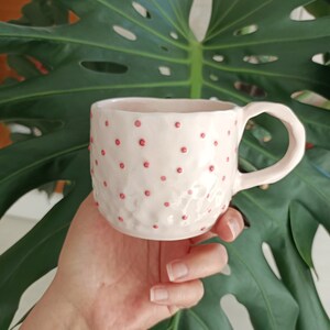 May include: A pink ceramic mug with a textured surface and pink polka dots.