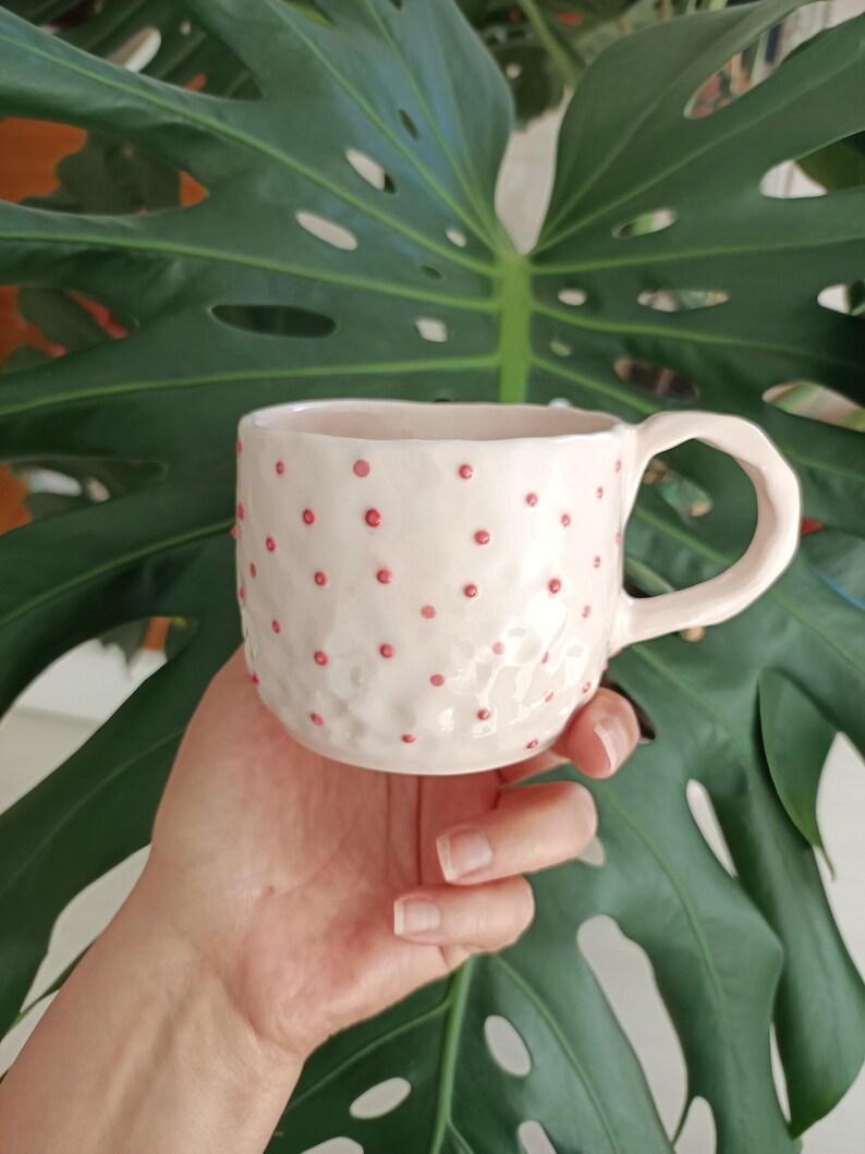 May include: A pink ceramic mug with a textured surface and pink polka dots.