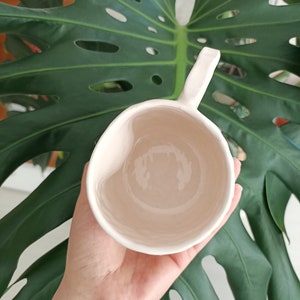 May include: A white ceramic mug with a handle. The mug is empty and has a smooth, glossy finish.
