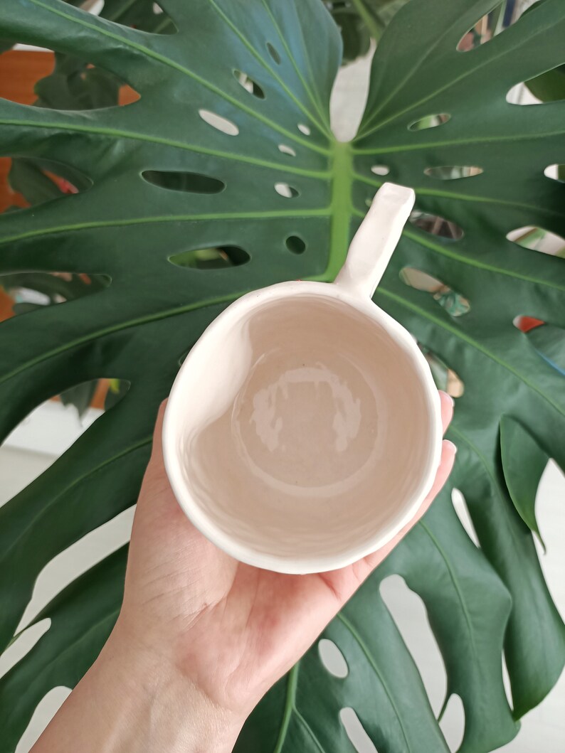 May include: A white ceramic mug with a handle. The mug is empty and has a smooth, glossy finish.