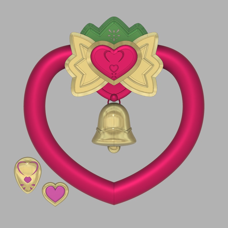 May include: A pink heart-shaped ring with a gold bell hanging from a green and gold bow with a heart in the center.