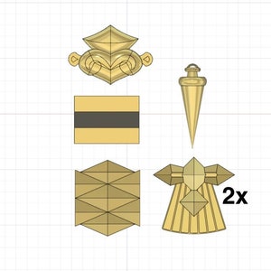 Puede incluir: Un conjunto de cinco piezas decorativas de metal de color dorado. El conjunto incluye una pieza con forma de corona, una pieza cuadrada con una franja negra, una pieza puntiaguda y dos piezas id&eacute;nticas con un dise&ntilde;o en forma de estrella. Las piezas con forma de estrella tienen una etiqueta 2x.