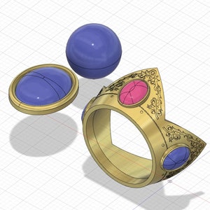 Peut inclure: Une bague dorée avec un motif de couronne, ornée de pierres précieuses roses et bleues. Une sphère bleue et une pierre précieuse ovale bleue sont également présentes. La bague présente des détails ornés et une finition polie.