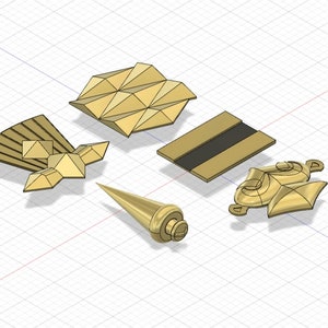 Puede incluir: Cinco adornos de metal de color dorado con dise&ntilde;os geom&eacute;tricos. Los adornos est&aacute;n dispuestos sobre un fondo de cuadr&iacute;cula blanca.
