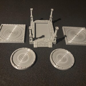 May include: A collection of gray 3D-printed components, including a central platform with decorative pillars and steps, two square platforms, and two circular platforms. The platforms feature a concentric circle design.