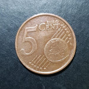 May include: A copper-colored 5 Euro cent coin with the inscription "EURO CENT" and a globe design.