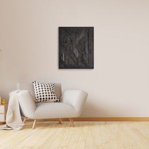 May include: A white armchair with a black and white patterned pillow sits in a room with a light wood floor. A black and white abstract geometric wall art hangs on the wall above the chair.