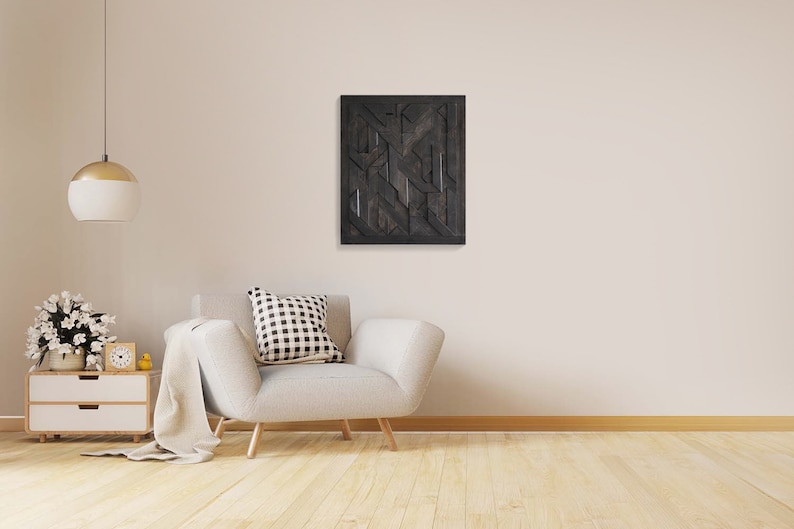 May include: A white armchair with a black and white patterned pillow sits in a room with a light wood floor. A black and white abstract geometric wall art hangs on the wall above the chair.