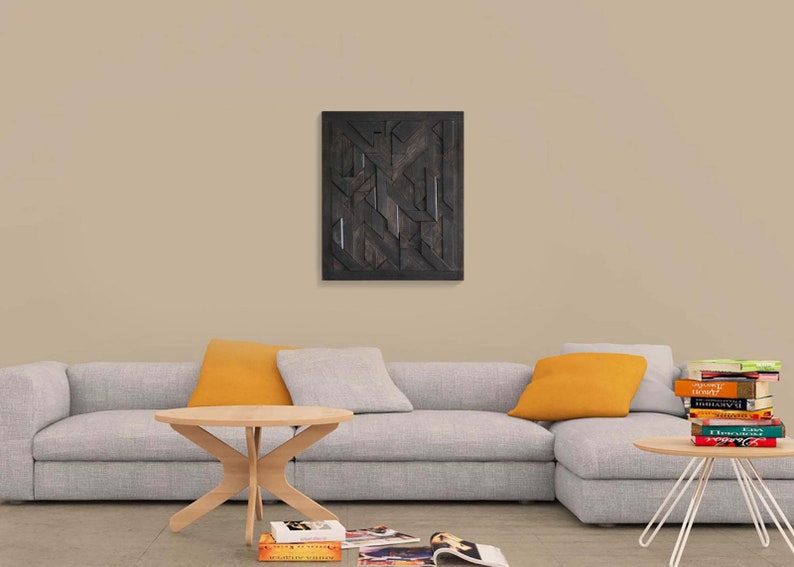 May include: A gray sectional sofa with two orange throw pillows, a wooden coffee table, and a stack of books on a metal side table. A black and white geometric wooden wall art hangs above the sofa.