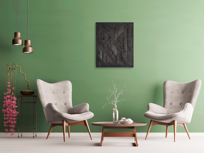 May include: Two beige armchairs with wooden legs face each other in a living room with a green wall. A black and brown geometric wall art hangs above a coffee table with a vase of white flowers.