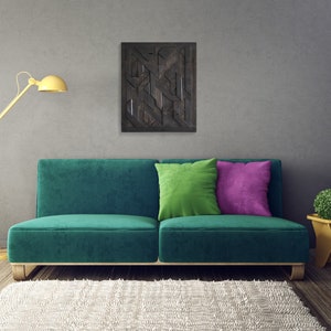 May include: A teal green sofa with two pillows, one green and one purple, sits in front of a gray wall with a black and white geometric wall art hanging above it. A yellow floor lamp is on the left side of the sofa and a small yellow side table with a green plant is on the right side of the sofa. A white fluffy rug is in front of the sofa.