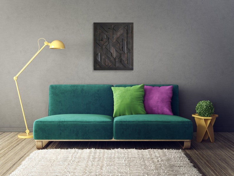 May include: A teal green sofa with two pillows, one green and one purple, sits in front of a gray wall with a black and white geometric wall art hanging above it. A yellow floor lamp is on the left side of the sofa and a small yellow side table with a green plant is on the right side of the sofa. A white fluffy rug is in front of the sofa.