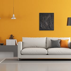May include: A white sofa with gray and orange throw pillows sits in a living room with a yellow wall, a gray wall, and a black and white geometric wall art piece. There are two pendant lights hanging from the ceiling and a floor lamp with a black shade.