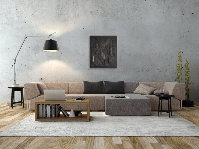 May include: A modern living room with a large sectional sofa in a light brown fabric. The sofa is arranged in an L-shape with a coffee table in the center. The coffee table has a wooden frame and two shelves. The room has a concrete wall with a black and white geometric art piece hanging on it. There is a floor lamp with a black shade in the corner of the room.