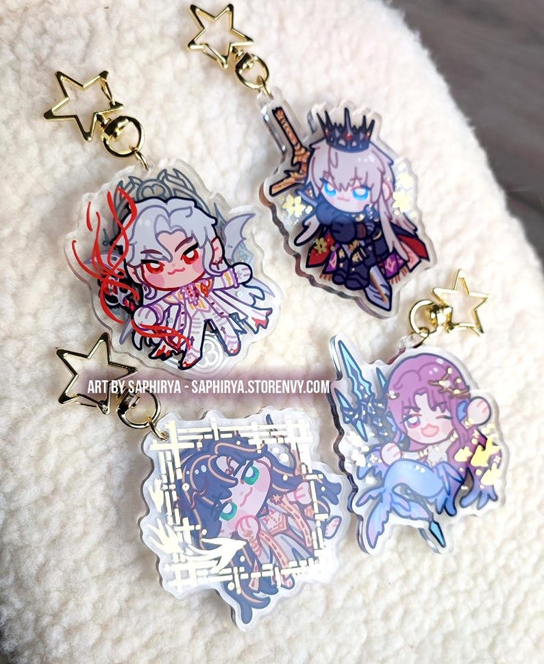 Puede incluir: Cuatro llaveros de acr&iacute;lico con personajes de estilo anime chibi y cierres dorados en forma de estrella. Los dise&ntilde;os incluyen una figura de pelo blanco, un personaje coronado con una espada, una figura de pelo oscuro en un marco y una sirena. El texto dice ART BY SAPHIRYA - SAPHIRYA.STORENVY.COM.