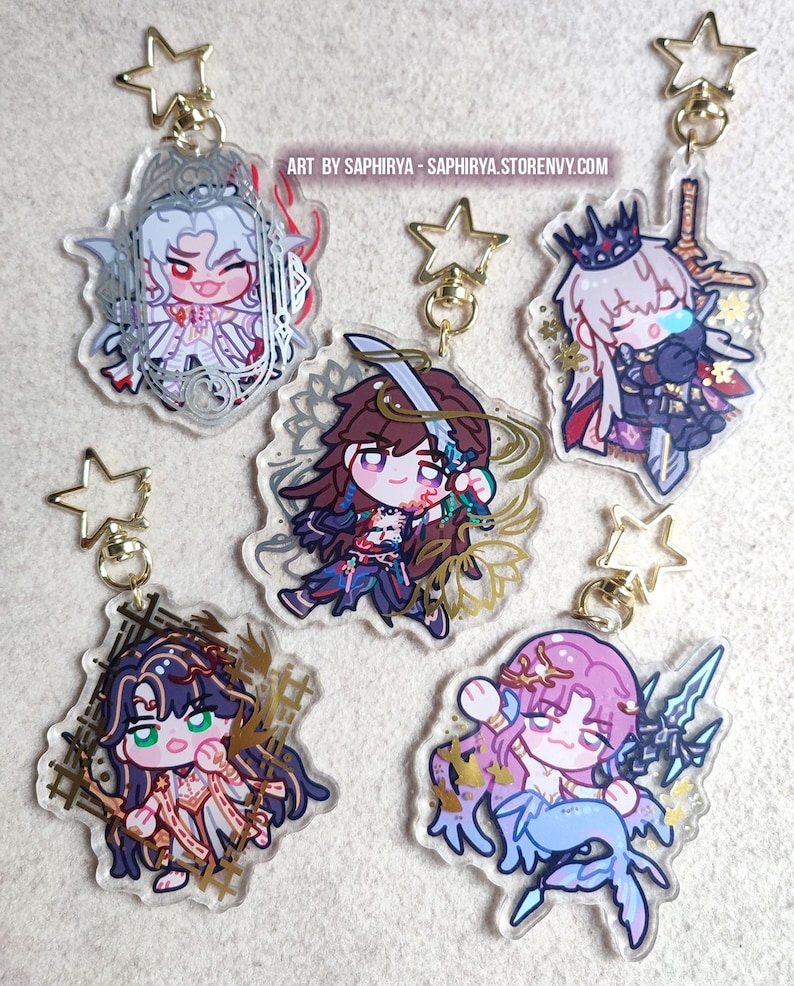 Puede incluir: Cinco llaveros de acr&iacute;lico transparente con personajes de estilo anime chibi y cierres dorados en forma de estrella. Cada dije muestra dise&ntilde;os de personajes &uacute;nicos con detalles intrincados y colores vivos. El texto ART BY SAPHIRYA - SAPHIRYA.STORENVY.COM es visible.