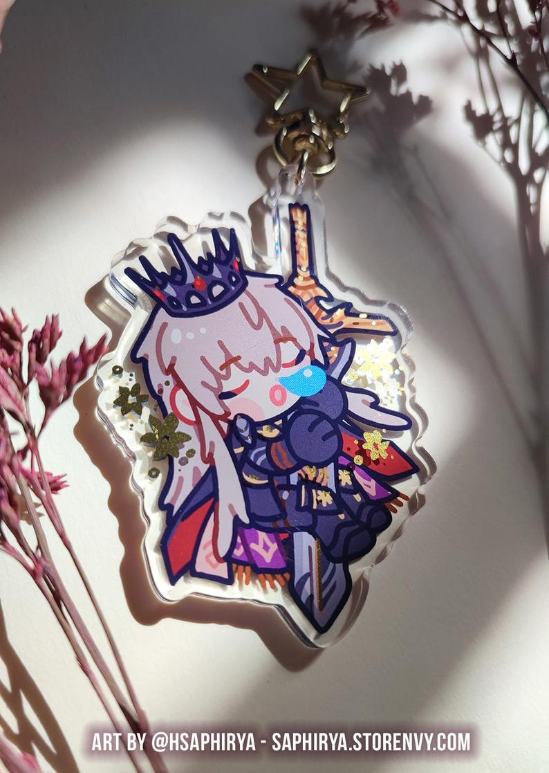 Puede incluir: Un llavero de acr&iacute;lico con un personaje chibi de largo cabello blanco y corona oscura, vistiendo una armadura morada y negra mientras sostiene una gran espada. El dije transparente contiene purpurina dorada en forma de estrella.