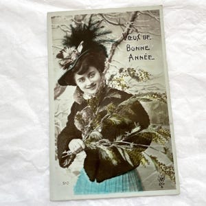 Anni '10 - Cartolina francese - Cartolina "Felice Anno Nuovo" - Giovane donna con rami di abete e mimosa e un cappello Belle Époque