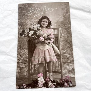 1910 – Francuska pocztówka z uśmiechniętą dziewczynką i kwiatami – „Bonne fête”