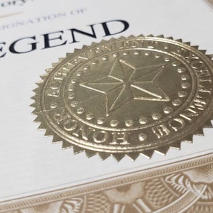 Puede incluir: Certificado con sello de l&aacute;mina dorada. El sello presenta una estrella y las palabras "ACHIEVEMENT EXCELLENCE HONOR". El certificado dice "WORLD LEGEND" en negrita negra. Borde decorativo.