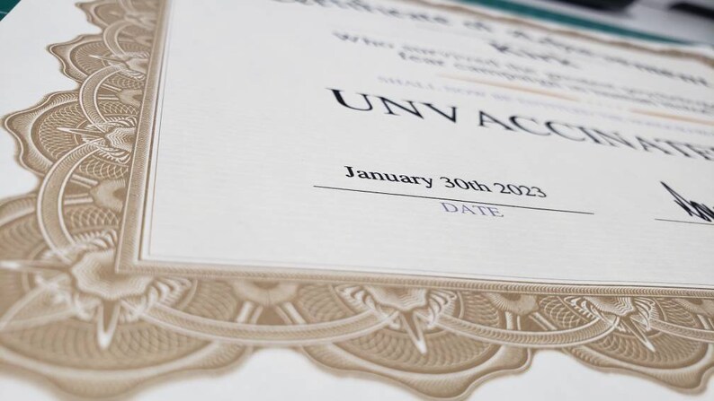 Puede incluir: Un certificado con bordes de filigrana decorativos de color beige y un fondo crema. El texto "UNV ACCINATED" se muestra de forma destacada, junto con la fecha "30 de enero de 2023". El certificado es probablemente un art&iacute;culo conmemorativo.