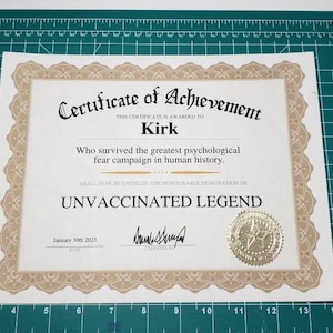 Puede incluir: Un certificado de logro con bordes ornamentados y un sello dorado. El texto dice "Certificado de Logro" y "Leyenda No Vacunada", con el nombre "Kirk" y la fecha "30 de enero de 2023". El certificado est&aacute; sobre una esterilla de corte verde.
