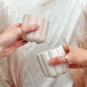 May include: Two white ceramic planters with a fluted design. The planters are held by two hands, one on each side.