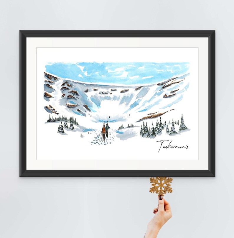 May include: A watercolour painting of a snowy mountain scene with two figures hiking up a trail. The painting is framed in black and has the text "Tuckerman's" in the bottom right corner.