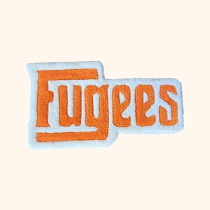Peut inclure: Patch brodé orange avec le mot "Fugees" sur un fond blanc.