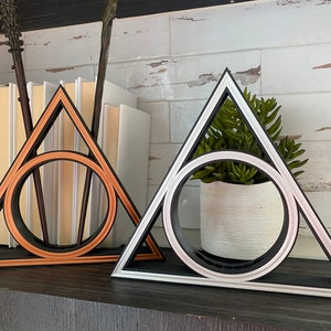May include: Two decorative triangle-shaped wall shelves with a circle in the center. The shelf on the left is copper colored and the shelf on the right is black with a silver trim.