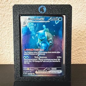Pode incluir: Uma carta colecionável Blastoise ex com 330 HP, apresentando a habilidade Solid Shell e o ataque Twin Cannons, exibida dentro de uma moldura retangular preta texturizada com um ícone de símbolo de energia de água azul no topo central.