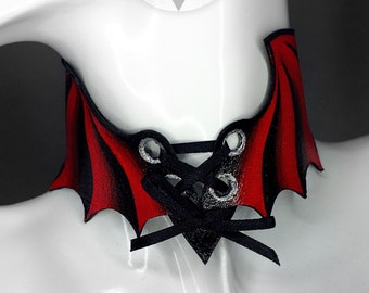 May include: Red leather choker with black lace-up detail and wing-shaped sides. The choker is on a white mannequin.