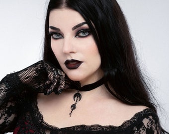 May include: A woman wearing a burgundy dress with black lace detailing and black lace gloves. She is wearing a black choker necklace with a crescent moon pendant. The text "Plamendura Art" is visible in the image.