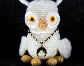 May include: White crocheted owl with yellow eyes and a gold chain necklace with a crescent moon pendant.