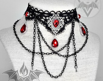 May include: A black lace choker necklace with a silver pendant and red gemstone drops. The necklace features multiple chains with dangling red gemstones.