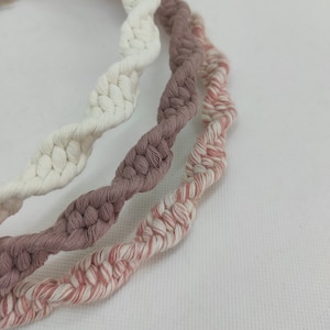 May include: Three braided cords in white, light brown, and pink and white. The cords are twisted together and have a wavy pattern.