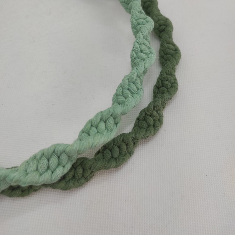 May include: Two strands of twisted cotton rope, one light green and one dark green, are shown against a white background.