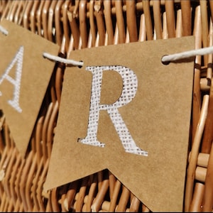 May include: A brown paper banner with the word "Party" spelled out in white letters. The banner is strung with white twine and is hanging on a wicker basket.