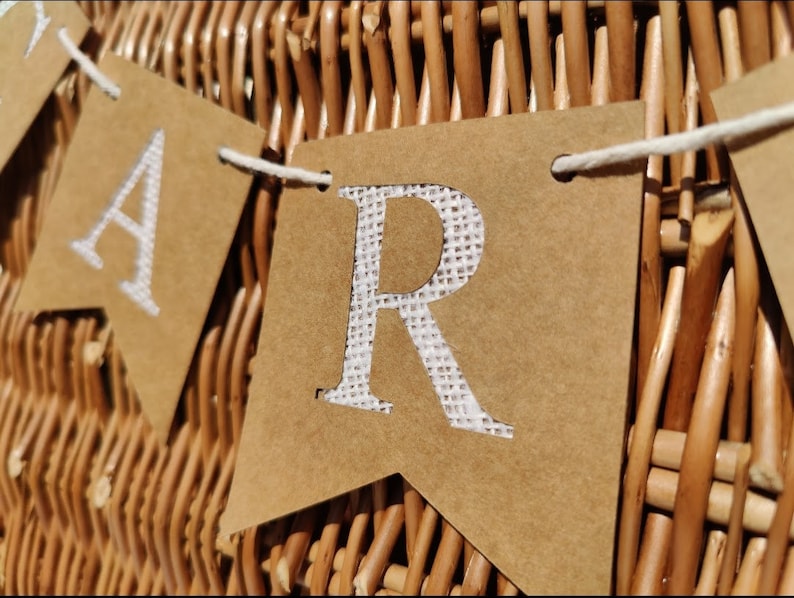 May include: A brown paper banner with the word "Party" spelled out in white letters. The banner is strung with white twine and is hanging on a wicker basket.