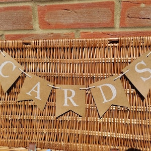 May include: A brown paper banner with white letters spelling "CARDS" hanging on a wicker basket.